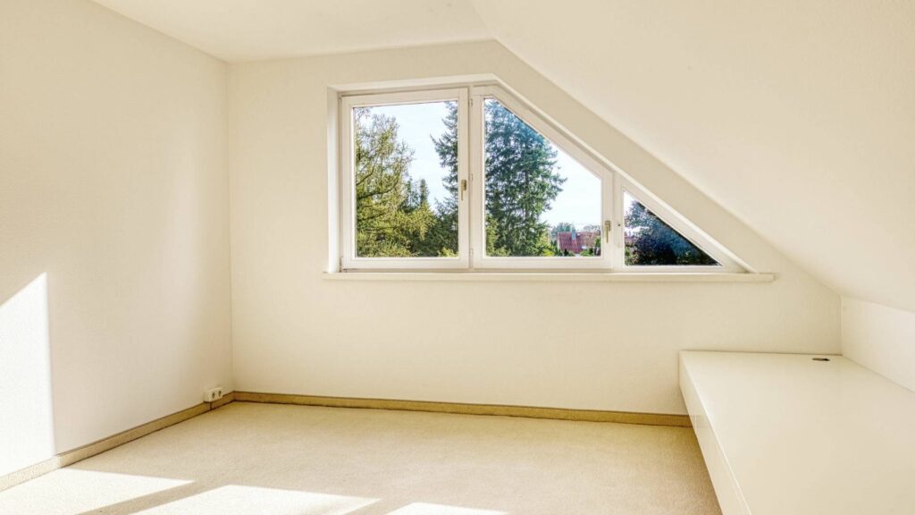 Leeres Dachgeschosszimmer des Lerchenauer Hauses mit schräger Decke und Fenster zum Garten