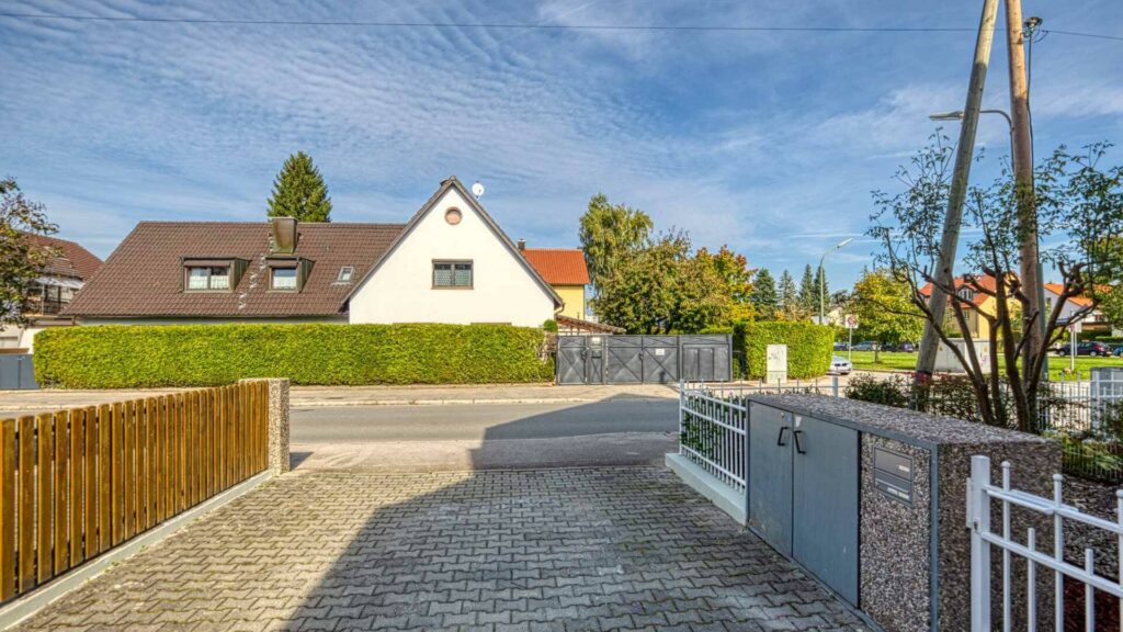 Gepflasterte Einfahrt mit Zaun und Blick auf ein Einfamilienhaus mit Satteldach in München-Lerchenau