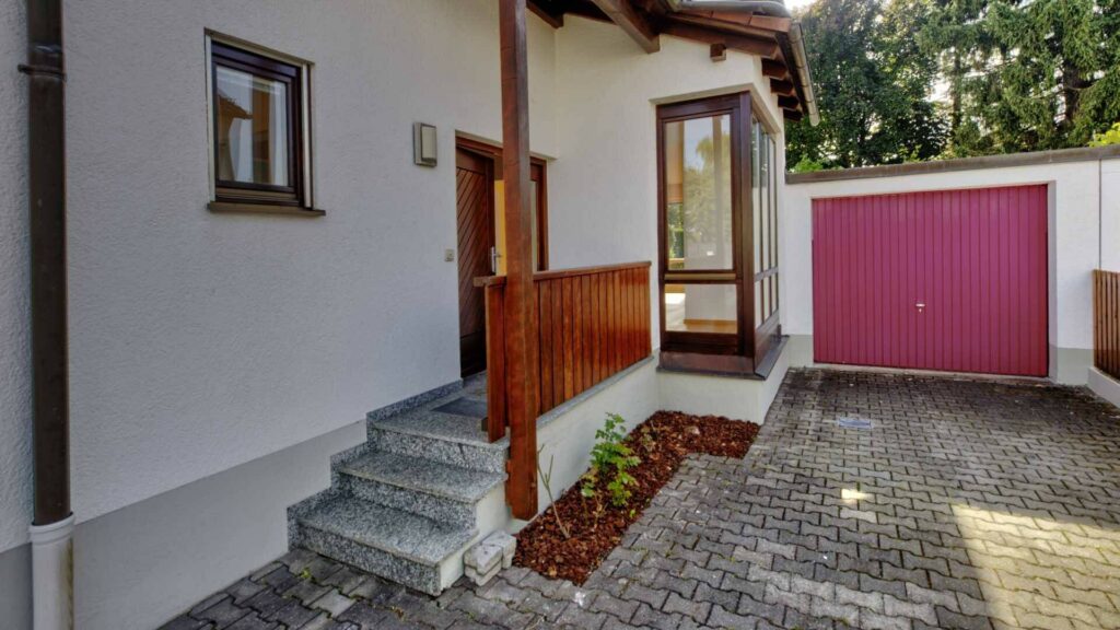 Eingangsbereich des Lerchenauer Hauses mit Steintreppe, Vordach und pinkfarbenem Garagentor