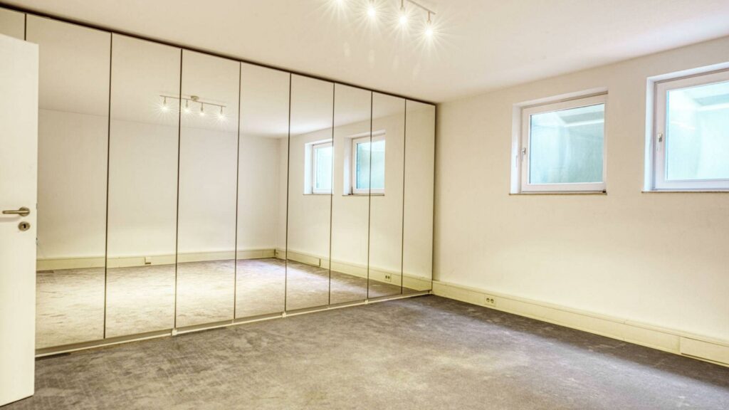 Heller Hobbyraum im Keller des Lerchenauer Hauses mit Spiegelschrankwand und Fenstern