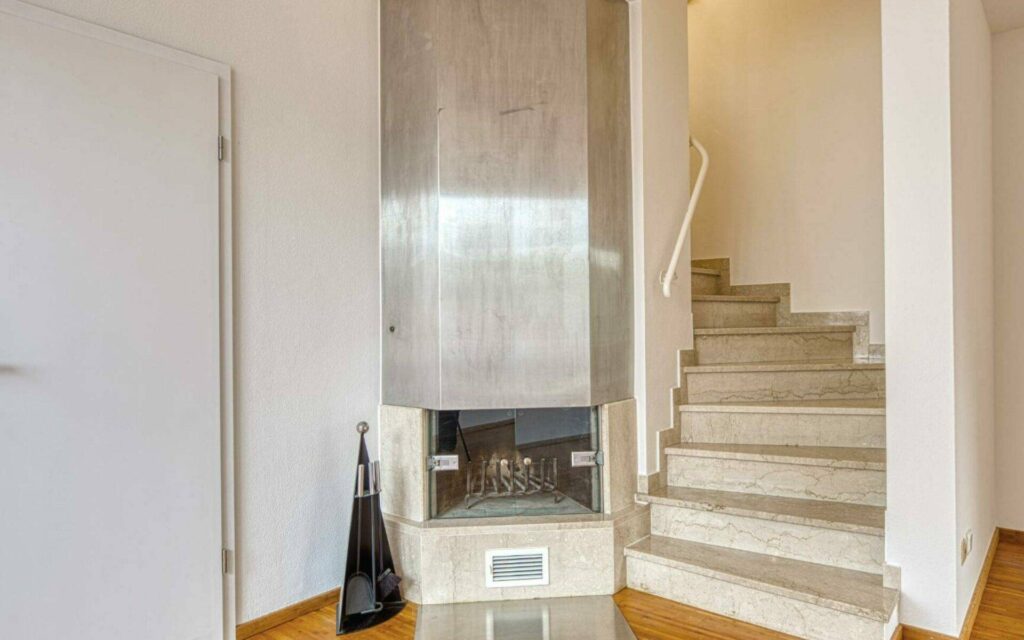 Eingebauter Kamin mit Steinboden neben einer hellen Natursteintreppe in einem Haus in München-Lerchenau.