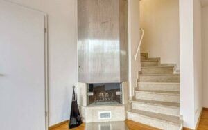Eingebauter Kamin mit Steinboden neben einer hellen Natursteintreppe in einem Haus in München-Lerchenau.