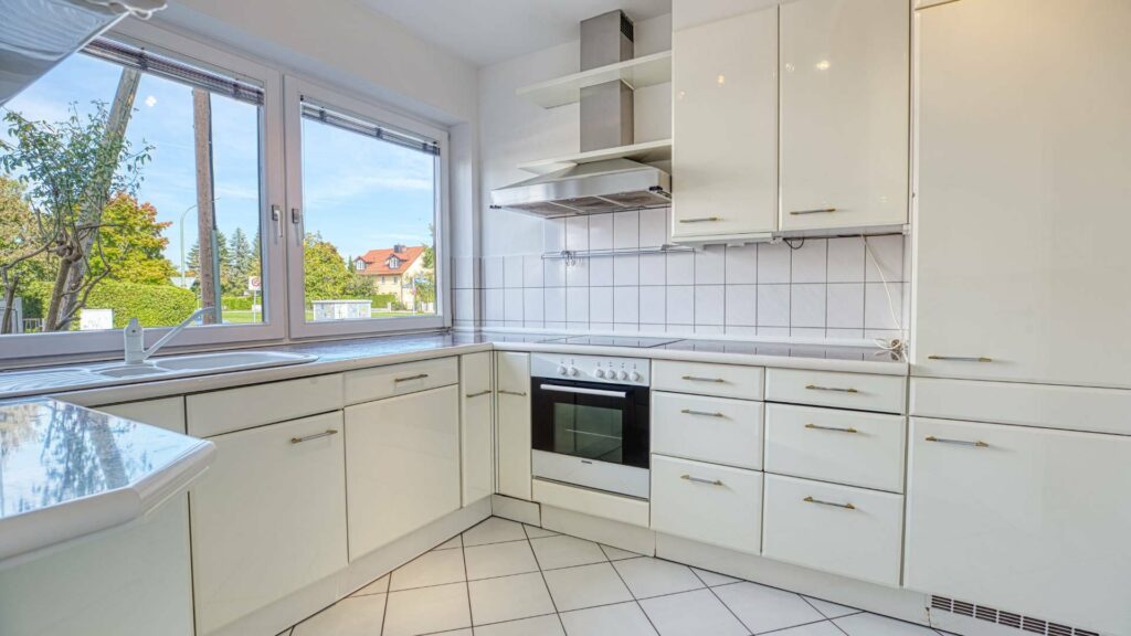 Cremefarbene Einbauküche des Lerchenauer Hauses mit Fliesenboden und Fenstern zum Garten