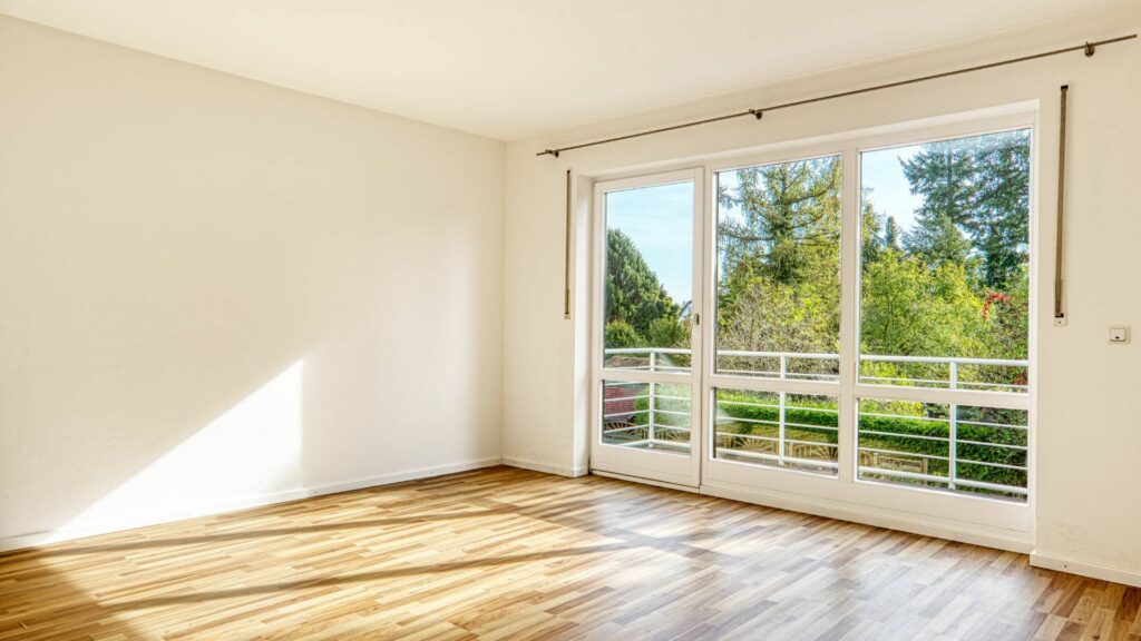Leeres Schlafzimmer des Lerchenauer Hauses mit Parkettboden und Blick auf Bäume vom Balkon aus