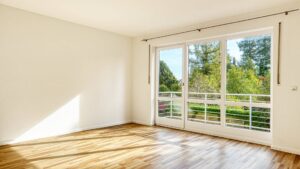 Leeres Schlafzimmer des Lerchenauer Hauses mit Parkettboden und Blick auf Bäume vom Balkon aus