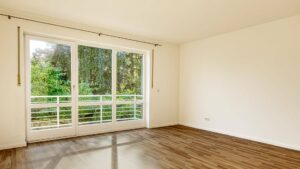 Leeres Schlafzimmer des Lerchenauer Hauses mit Parkettboden und Balkontür mit Geländer