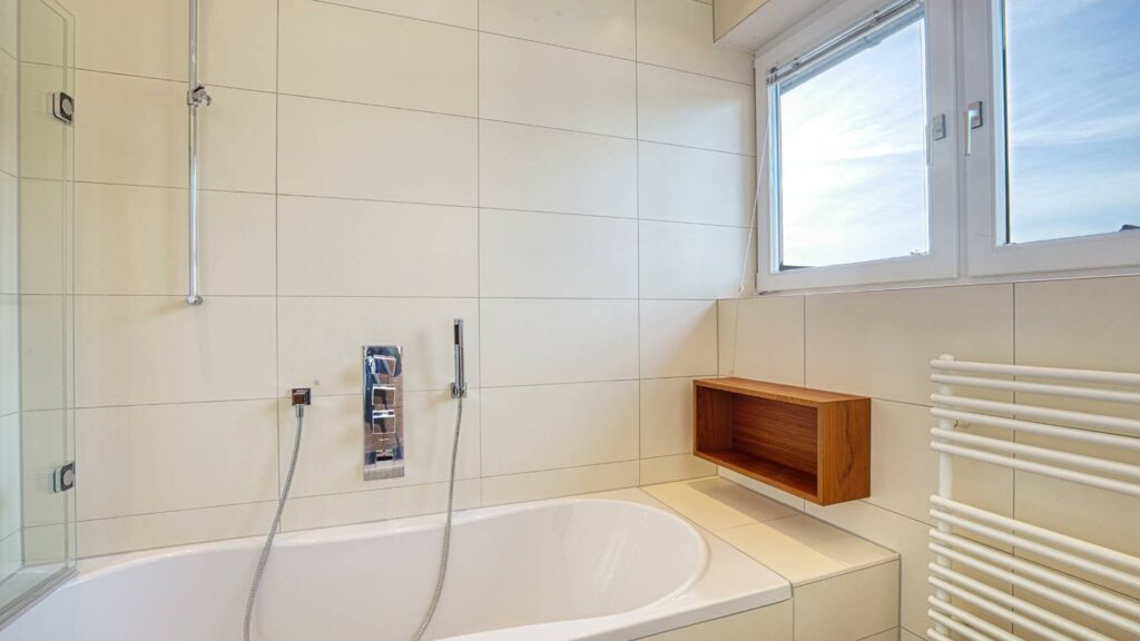 Badezimmer des Lerchenauer Hauses mit Badewanne, Glasabtrennung und Handtuchheizkörper