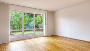 Leeres Wohnzimmer des Lerchenauer Hauses mit Parkettboden und breiter Fensterfront zum Garten