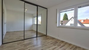 Leeres Zimmer im Obergeschoss des Lerchenauer Hauses mit Parkettboden und Spiegelschranktür
