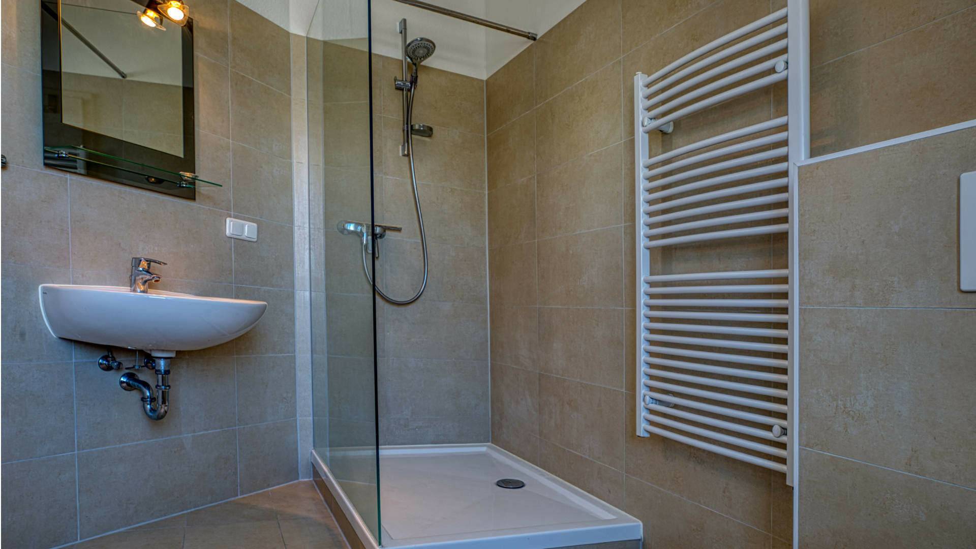 Kleines Badezimmer mit Glasdusche, Waschbecken und Heizkörper mit Handtuchhalter in einer Wohnung in der Maxvorstadt München