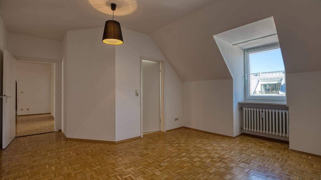 Leeres Zimmer mit Dachschräge, Parkettboden und Blick auf den Flur in einer Dachgeschosswohnung in der Maxvorstadt München