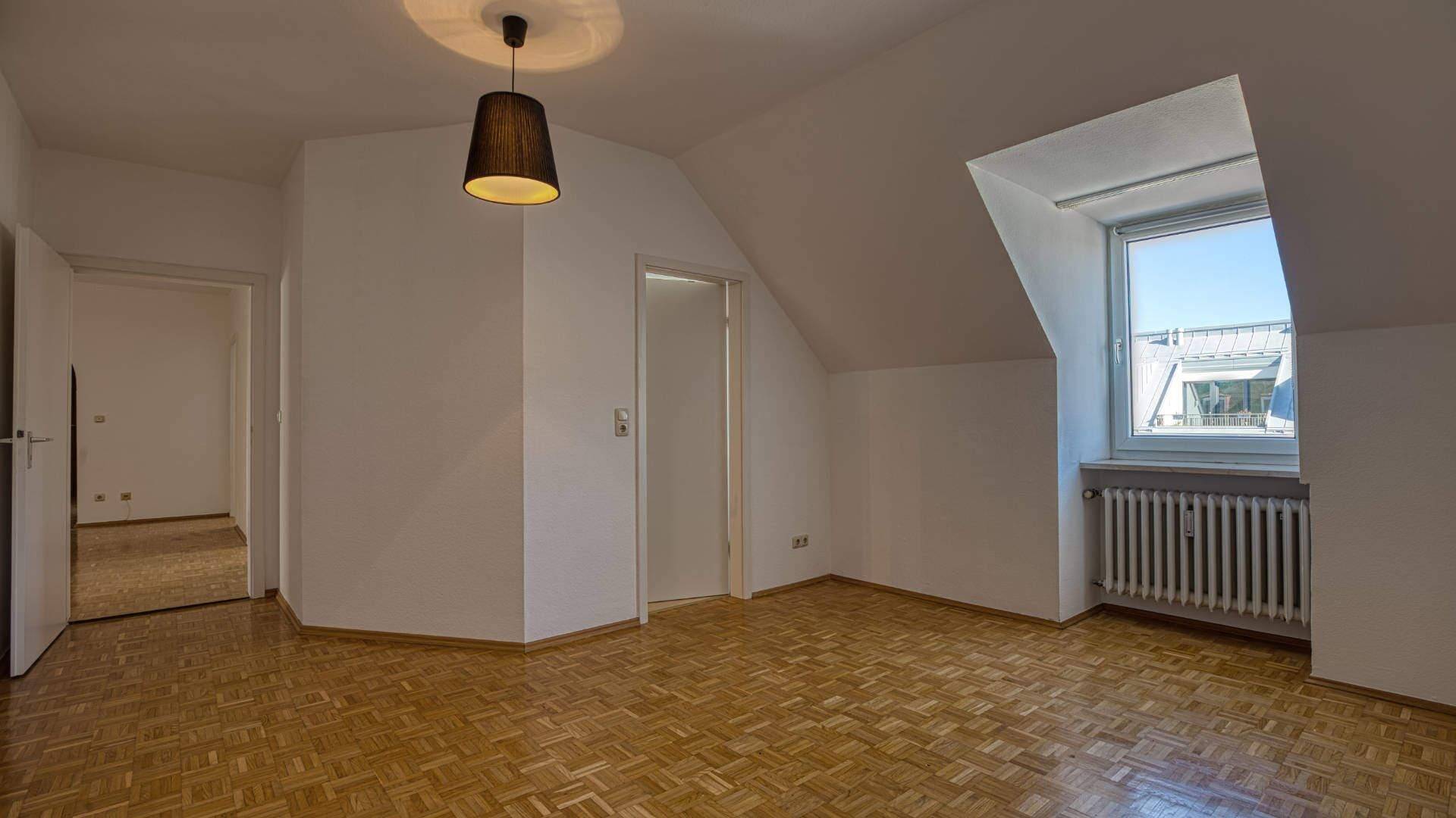 Leeres Zimmer mit Dachschräge, Parkettboden und Blick auf den Flur in einer Dachgeschosswohnung in der Maxvorstadt München