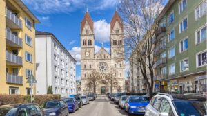 Straße mit parkenden Autos und Blick auf eine Kirche zwischen Wohnhäusern im Stadtviertel Maxvorstadt München