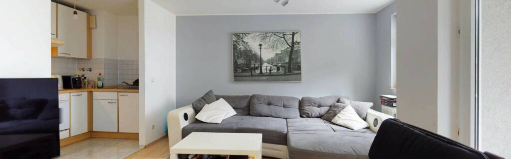 Offener Wohnbereich mit grauer Couch, Sitzkissen, Couchtisch und angrenzender Küchenzeile in einer Moosacher Wohnung.
