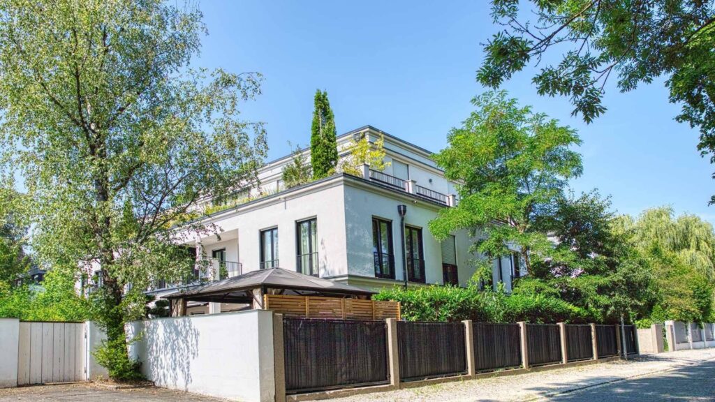 Weiße Stadtvilla mit umzäuntem Vorgarten und altem Baumbestand