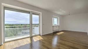 Unmöbliertes Zimmer mit Parkettboden, großem Fenster und Balkontür, Blick auf München-Obergiesing im Hintergrund.