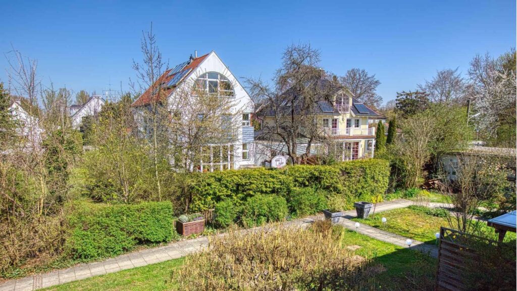 Blick über einen Garten auf ein weißes Landhaus mit Spitzdach nahe dem Reihenhaus in Obermenzing.