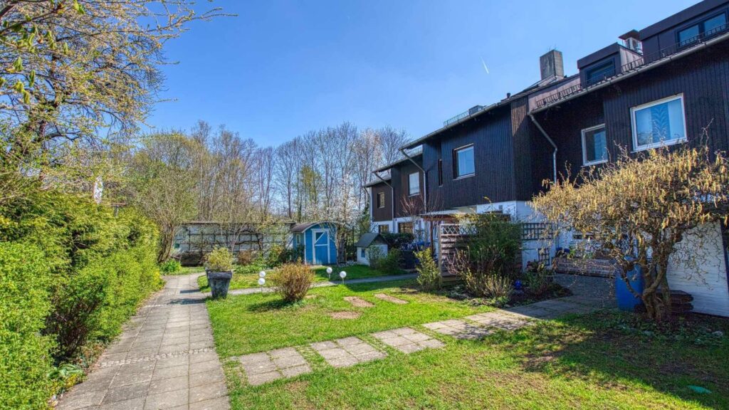 Reihenhaus mit dunkler Fassade, gepflastertem Weg und Frühlingsgarten in München-Obermenzing.