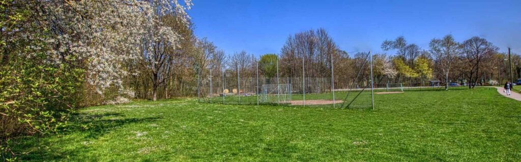 Grünfläche mit blühenden Sträuchern und Sportplatz in der Nachbarschaft des Reihenhauses in Obermenzing.