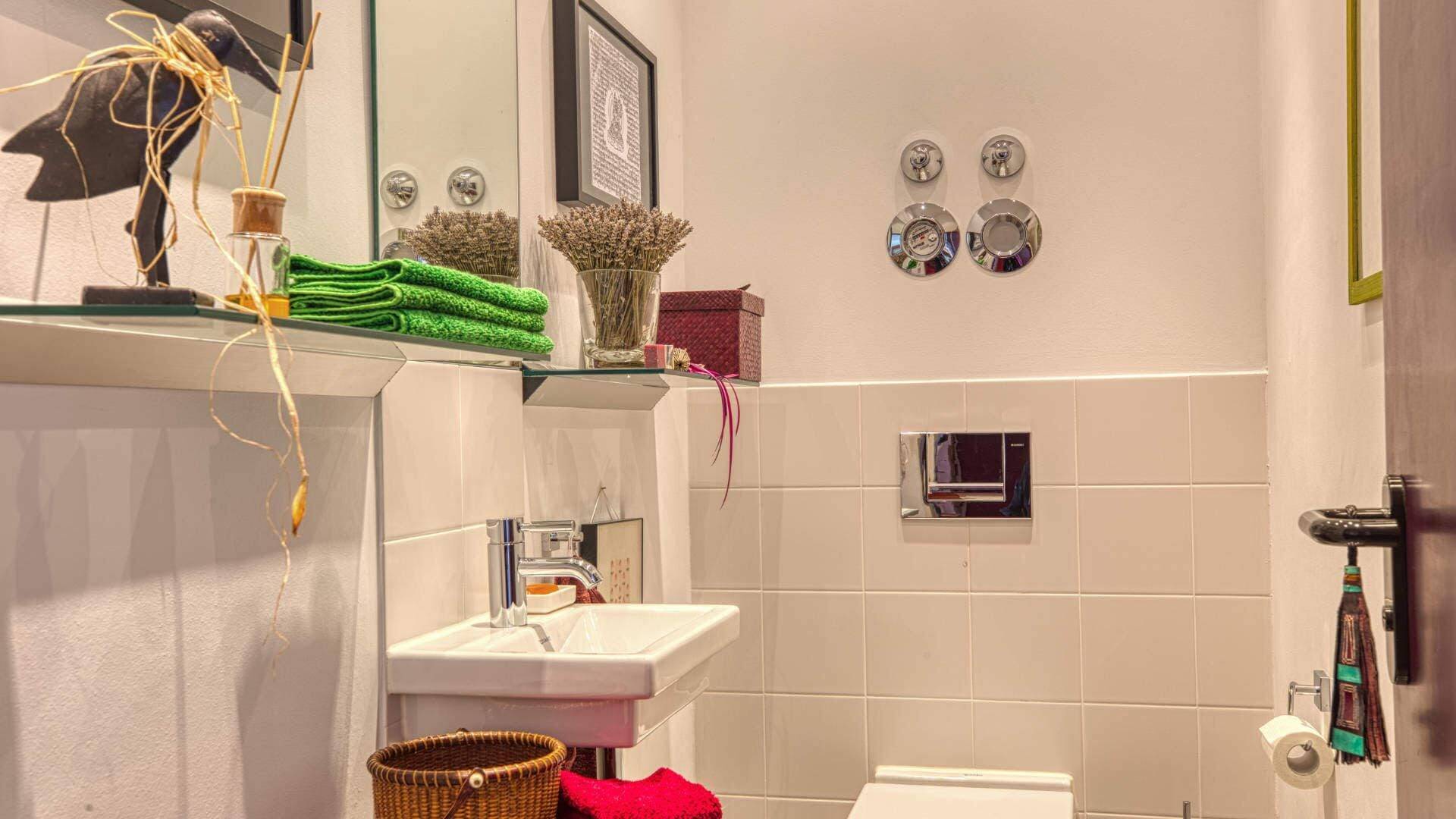 Modern bathroom in Obermenzing with sink, toilet and decorative shelf with candle holder and flowers on tiled wall