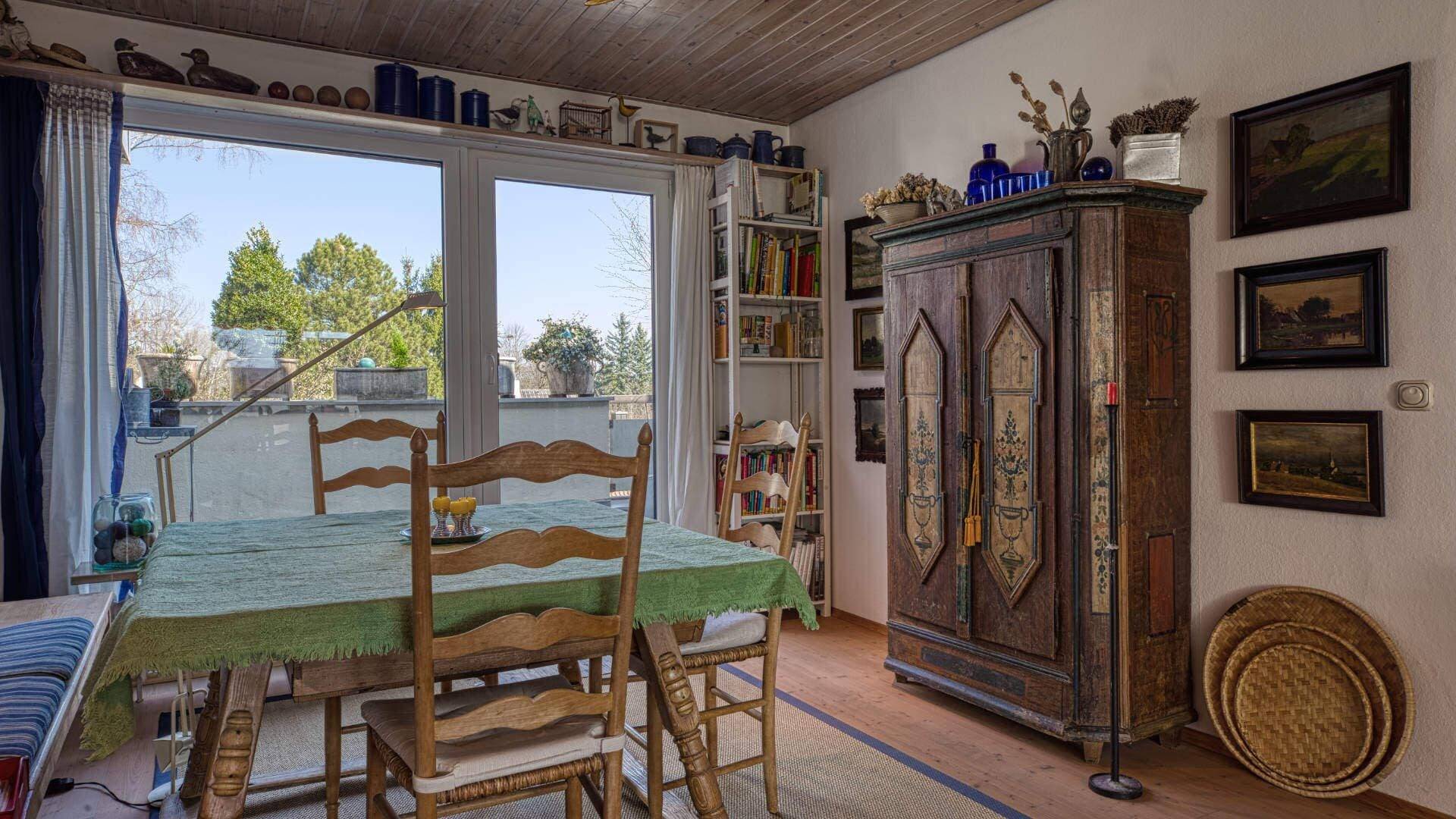 Cozy dining area with wooden table, chairs and antique farmhouse cabinet in front of a large window in an apartment in Obermenzing