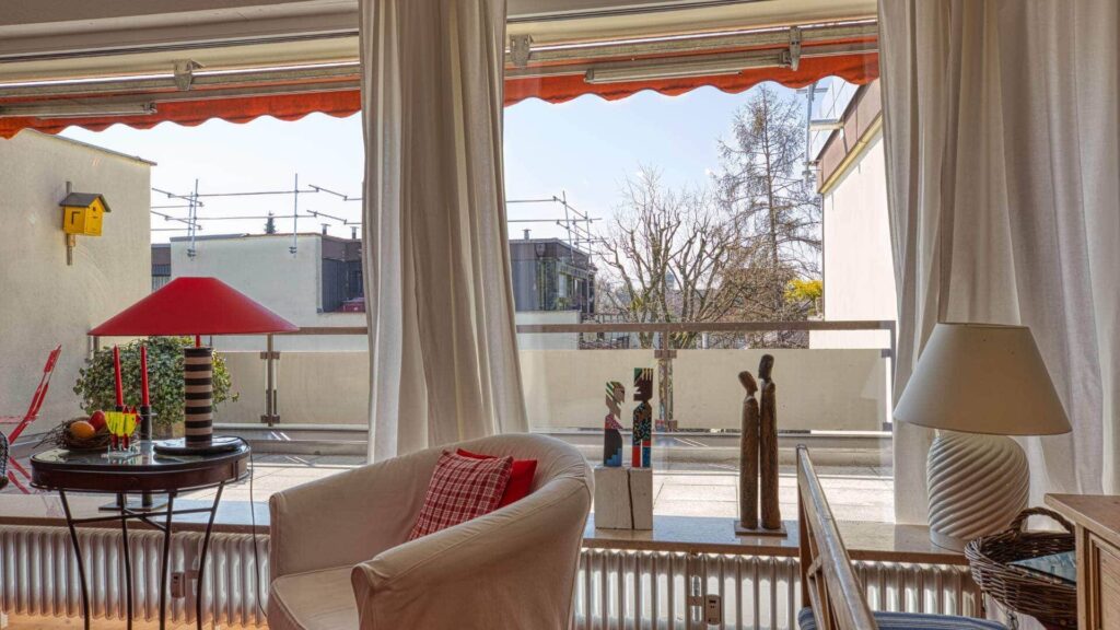Überdachter Balkon einer Wohnung in Obermenzing mit weißen Gardinen, Markise, rotem Sonnenschirm und dekorativen Figuren