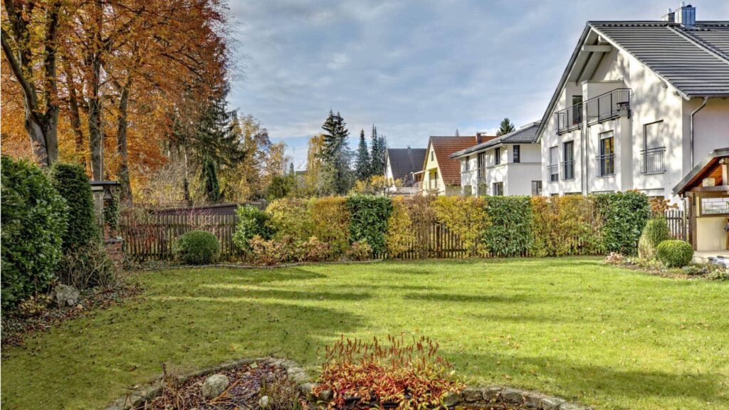 Grüne Rasenfläche des Grundstücks in Obersendling mit herbstlicher Villa im Hintergrund