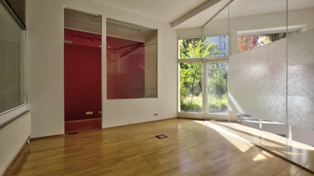 Empty space with red accent wall, wooden floor and large window front in an apartment on Orleansplatz, Munich