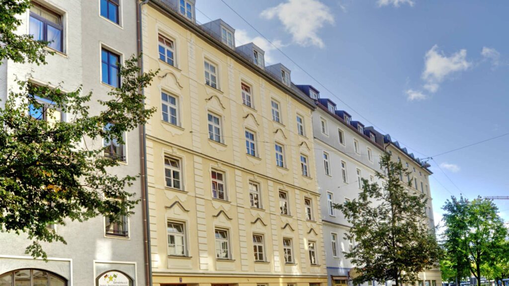 Historical old building facade with blue window shutters and trees in a street near Ostbahnhof in Munich