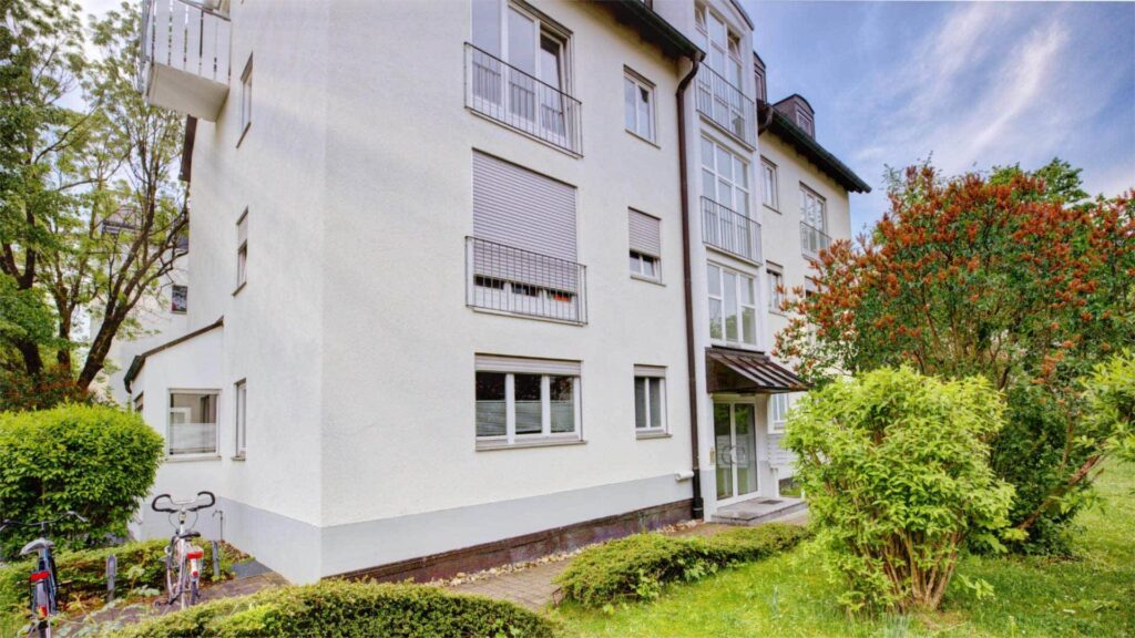 White apartment building with covered entrance, balconies and green area in Munich-Perlach.