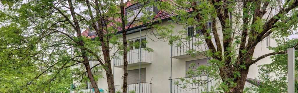 Facade with balconies behind dense tree growth at a residential building in Munich-Perlach.