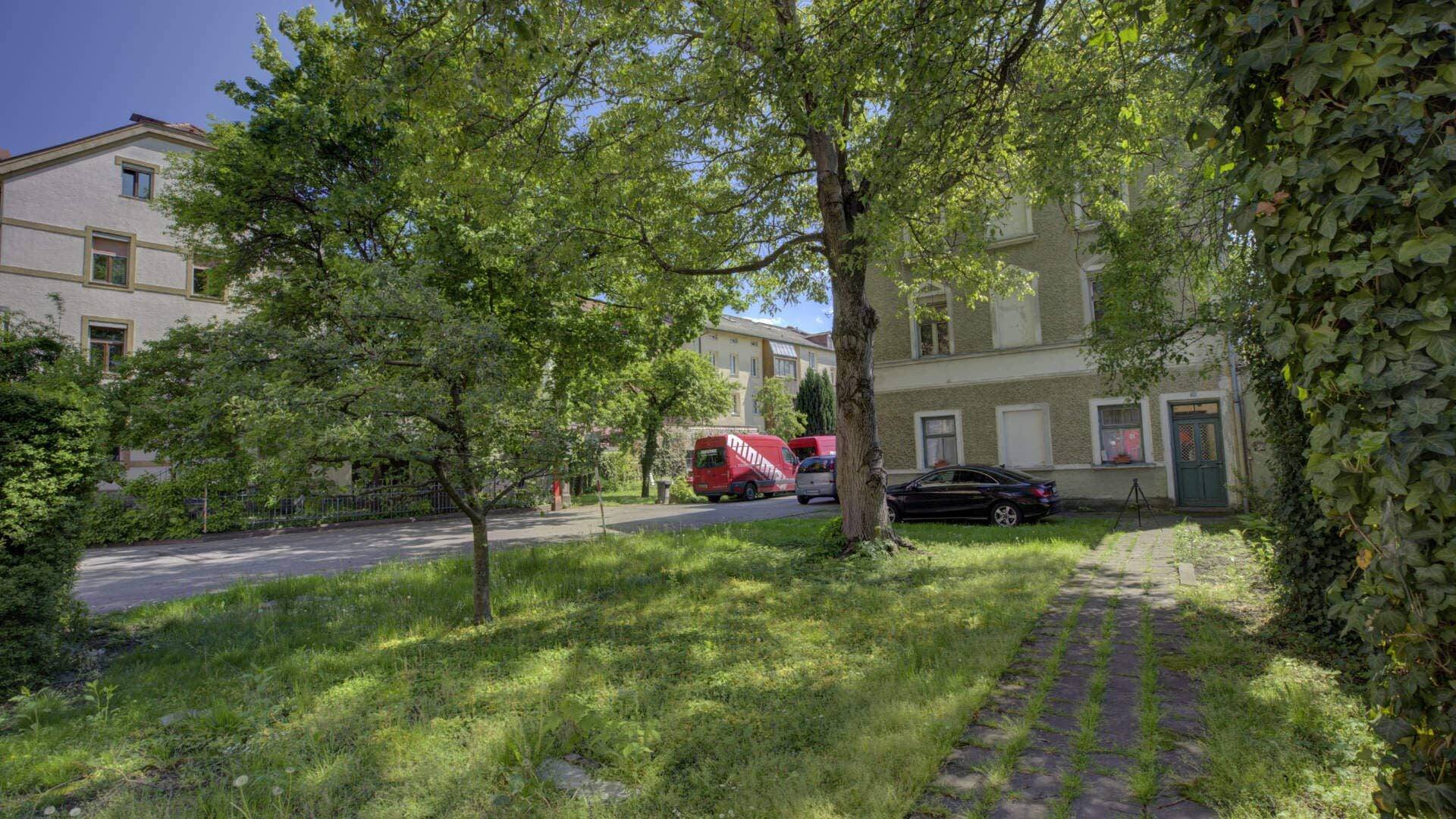 Grasbewachsene Zufahrt mit Bäumen und parkenden Autos vor einem Wohnhaus auf dem Grundstück in Rosenheim.