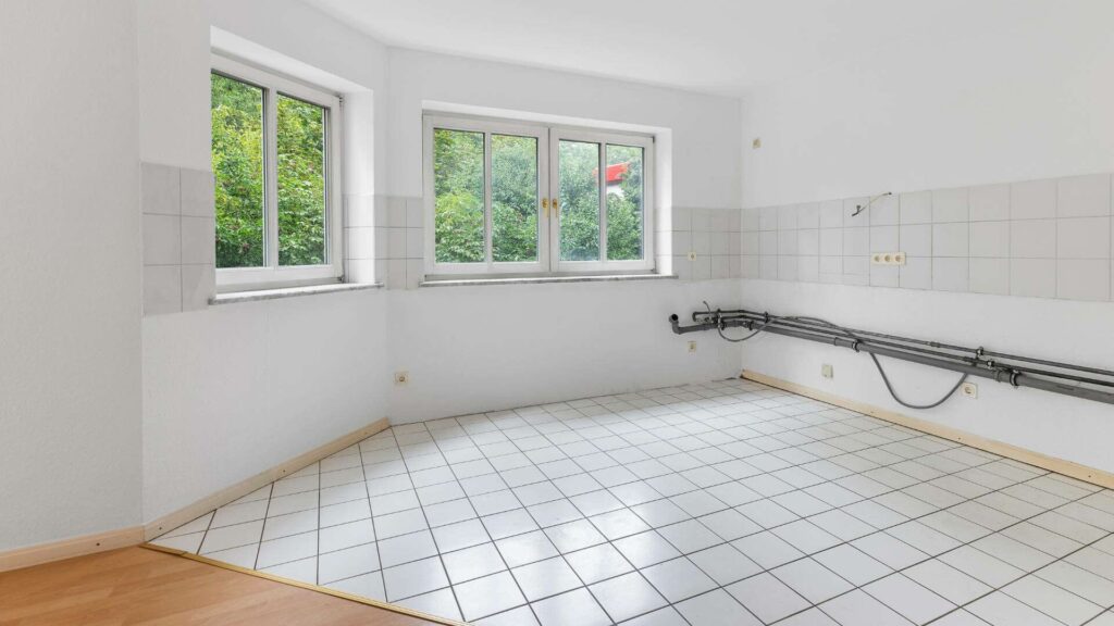 Empty kitchen of the Schwabing apartment with two windows facing the garden and tiled floor