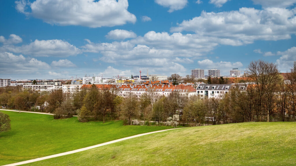 Wide green space with a view of the rooftops of Munich-Schwabing under a blue sky