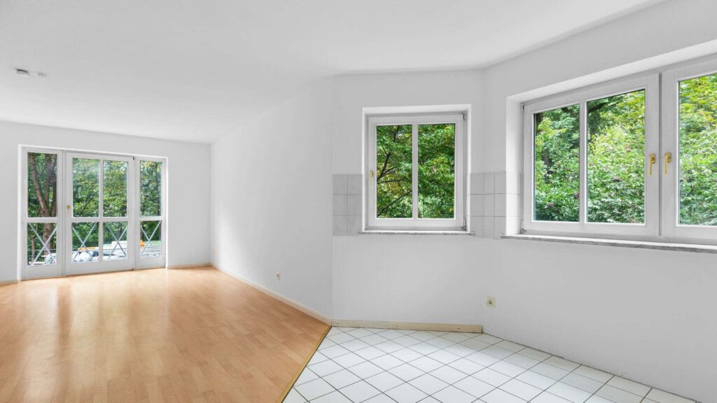 Empty corner living room of the Schwabing apartment with parquet and tile flooring and windows on two sides