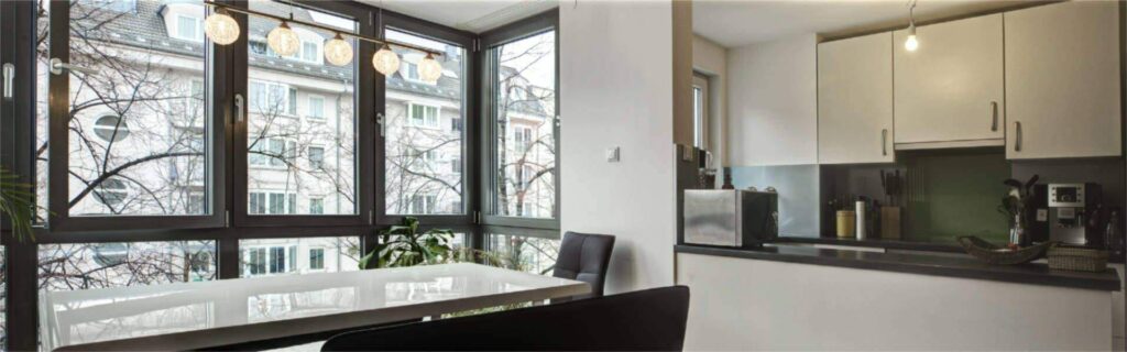 Esstisch vor großer Fensterfront eines Altbaus und angrenzende offene Küche in einer Wohnung in Sendling