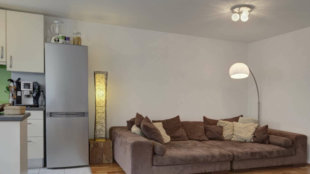 Wohnbereich mit Sofa und Küchenzeile mit Kühlschrank in einer Wohnung in München-Sendling