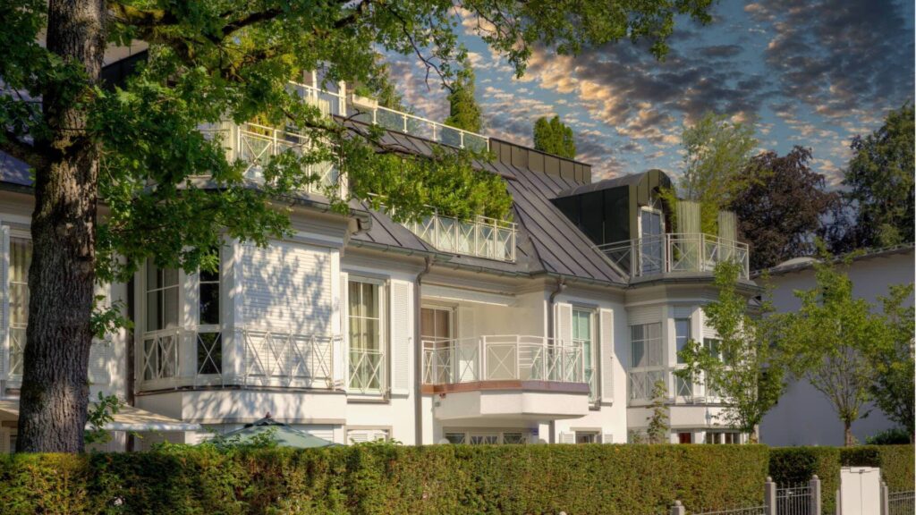 Weiße Villa mit mehreren Balkonen und Hecke unter dramatischem Abendhimmel – Symbolbild zur Spekulationssteuer beim Immobilienverkauf