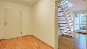 Helle Diele mit weißer Wandfläche, Parkettboden und offener Treppe in einer Wohnung in Thalkirchen.