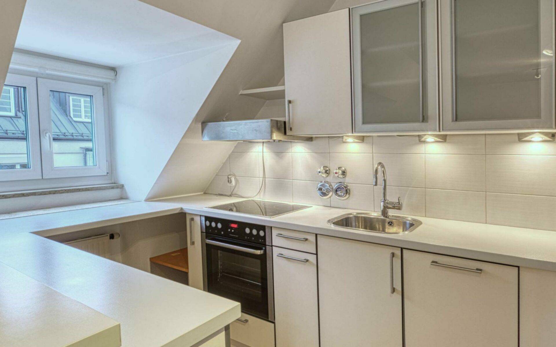 Helle Einbauküche mit U-Form, Dachschräge und Fenster in einer Dachgeschosswohnung in Thalkirchen.