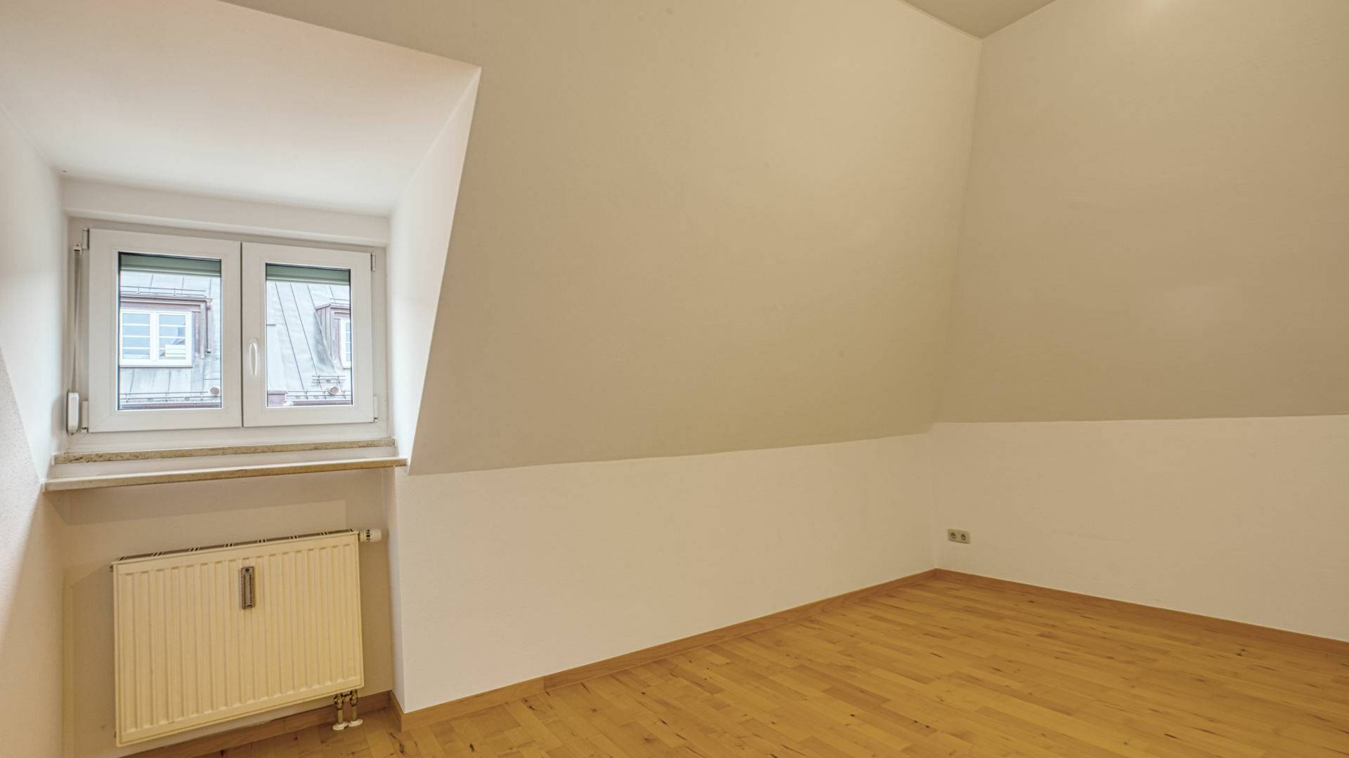 Unmöbliertes Zimmer mit Dachschräge, Dachfenster und Heizkörper in einer Wohnung in München-Thalkirchen