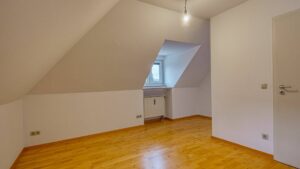 Unmöbliertes Zimmer mit steiler Dachschräge und Parkettboden in einer Wohnung in München-Thalkirchen