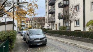Kopfsteinpflasterstraße mit parkenden Fahrzeugen und Wohnhäusern im Herbst in München-Thalkirchen.