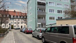 Straßenzug mit historischen und modernen Wohnhäusern sowie parkenden Autos in München-Thalkirchen.