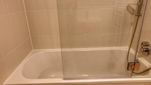 Nahaufnahme einer gefliesten Badewanne mit Glasabtrennung und Duschbrause in einer Wohnung in München-Thalkirchen