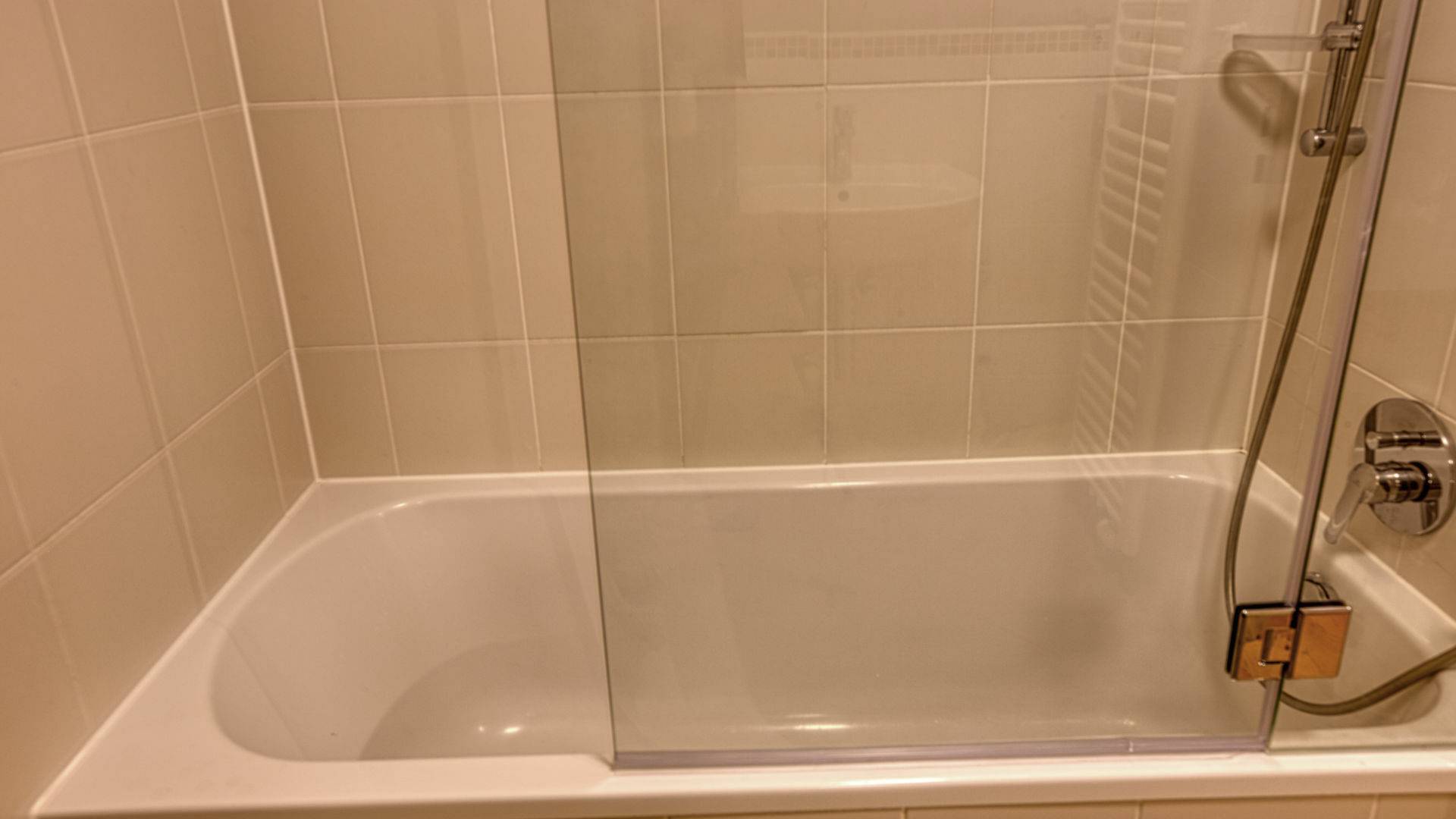 Nahaufnahme einer gefliesten Badewanne mit Glasabtrennung und Duschbrause in einer Wohnung in München-Thalkirchen