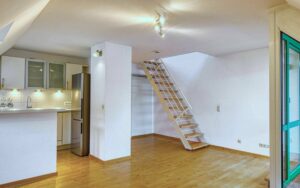 Open living area with kitchenette, wooden staircase and parquet floor in an apartment in Thalkirchen.