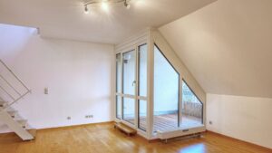 Leerer Wohnraum mit Dachschräge, Parkettboden und Terrassentür in einer Wohnung in Thalkirchen.