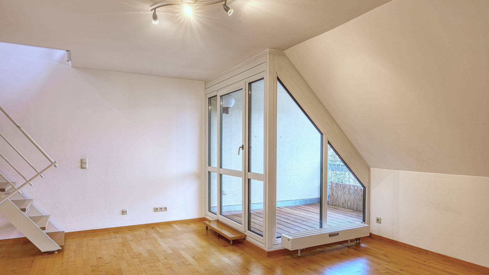 Leerer Wohnraum mit Dachschräge, Parkettboden und Terrassentür in einer Wohnung in Thalkirchen.