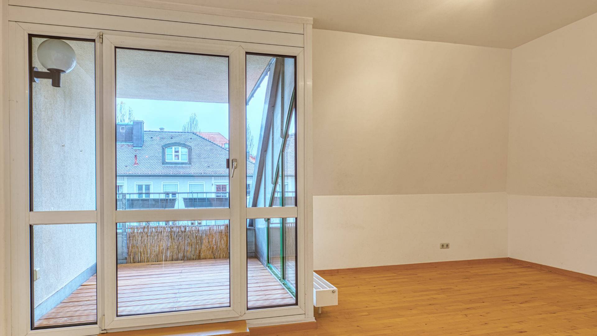Leeres Wohnzimmer mit Parkettboden und Zugang zur Dachterrasse mit Blick über die Dächer in Thalkirchen.